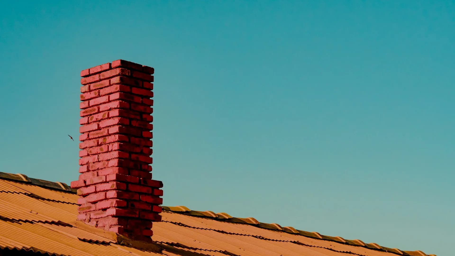 A brick chimney rising from a corrugated roof against an open sky